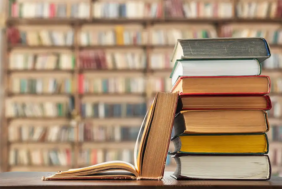 A stack of books resting on a wooden table inside a library