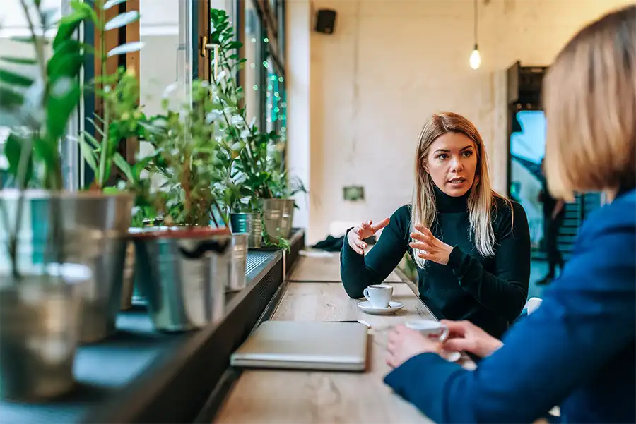 Two women sitting at a coffee shop bar having a conversation